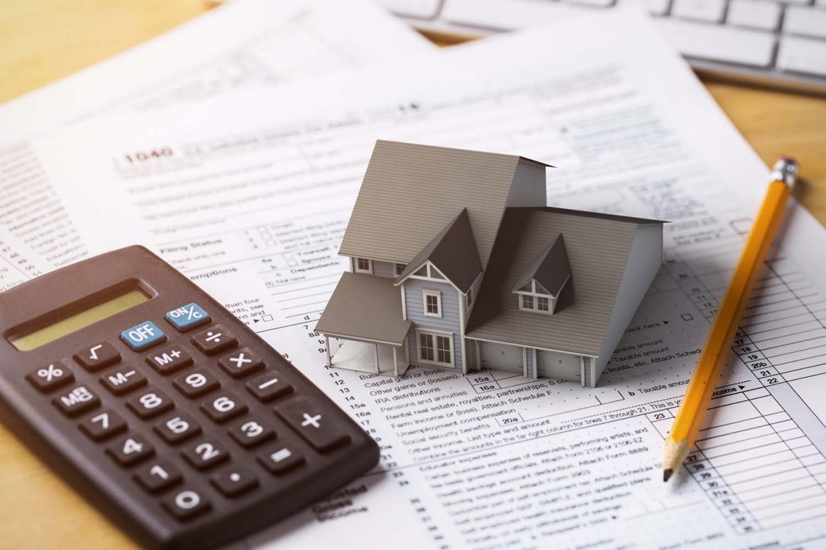 A small house on a tablet with a calculator and a pencil